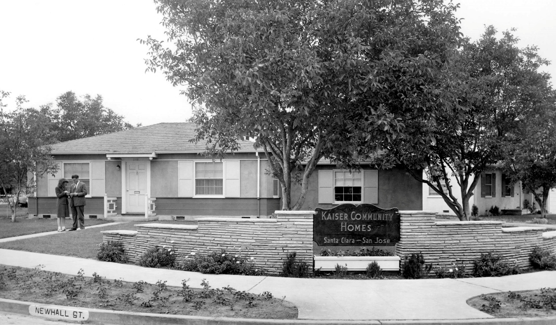 Historical image of a house in a subdivision. A man and woman are standing in the walkway.