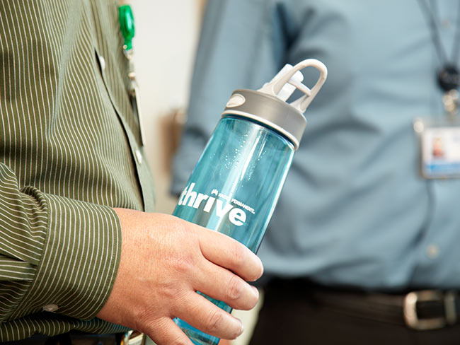 man's hand holding water bottle branded with Thrive