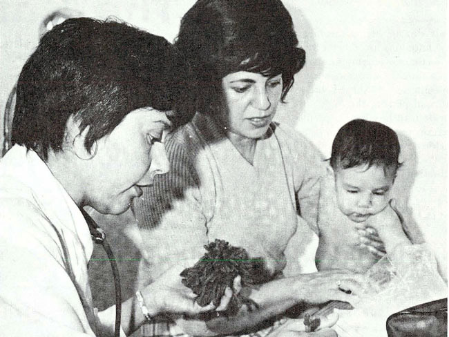 woman conducting a medical exam on a baby who's being held by its mother