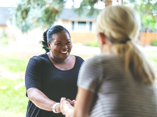 2 women greeting each other in a doorway to a home