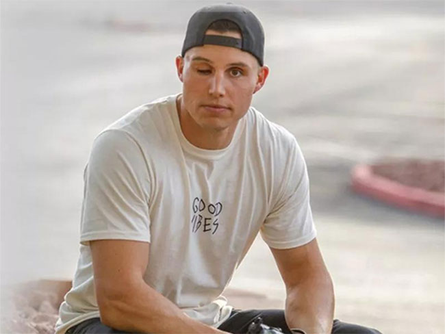 Drew Robinson sitting outdoors wearing baseball cap with the words "good vibes"