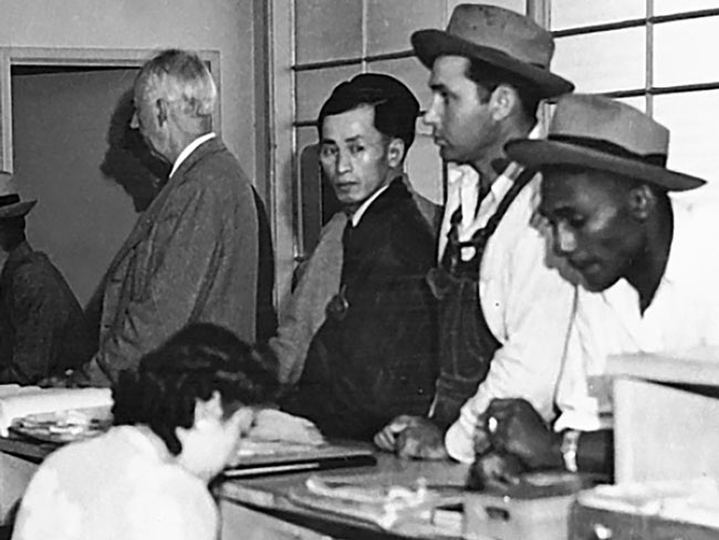 Woman seated behind desk with 4 men standing in front