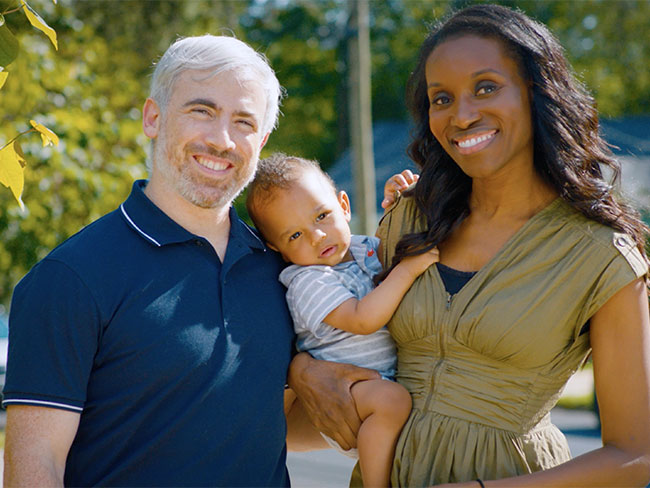 man and woman holding baby standing outdoors smiling