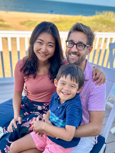 young boy with his parents sitting on a deck near the ocean