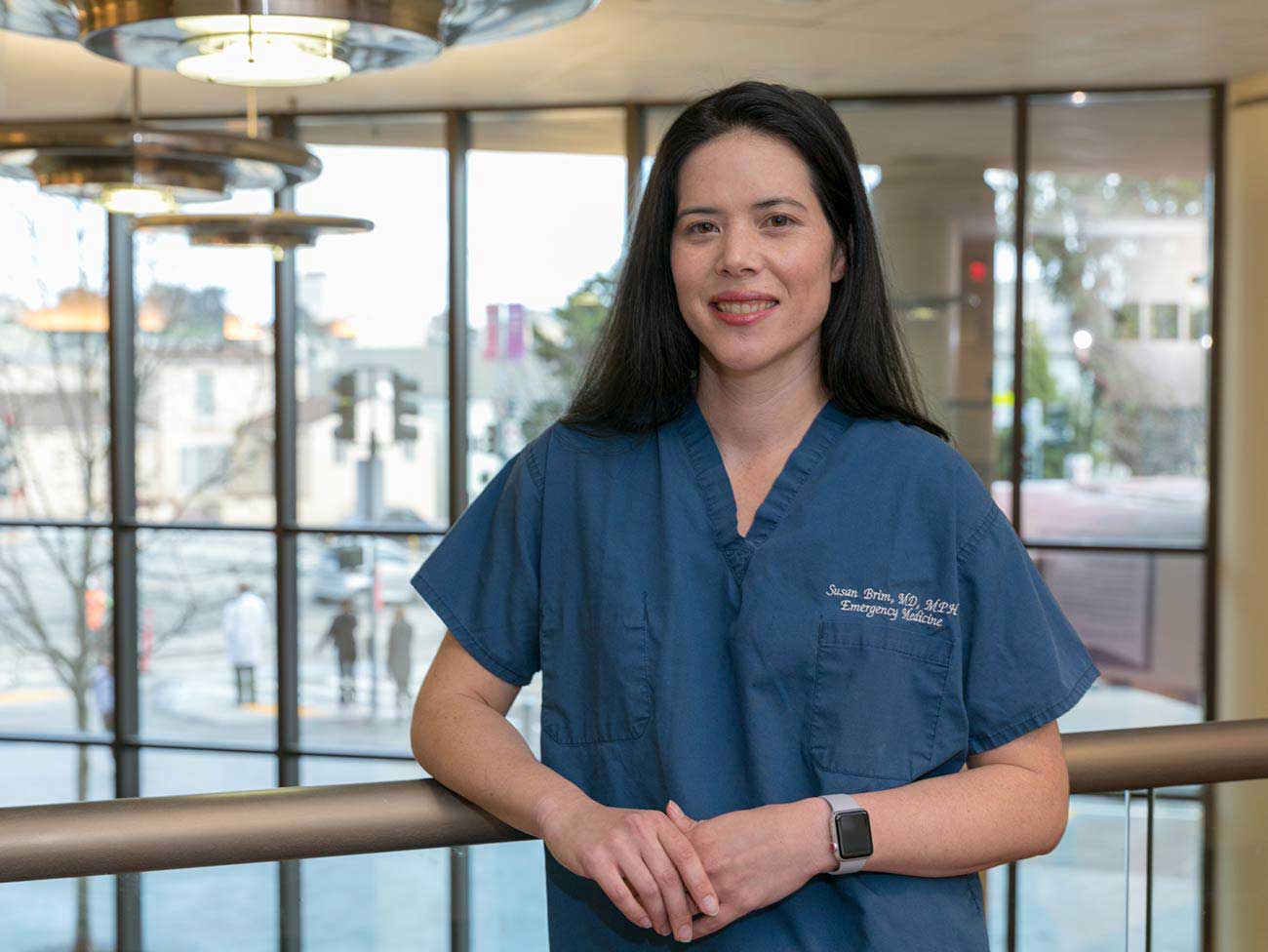 Susan Brim standing inside medical building wearing medical scrubs and smiling