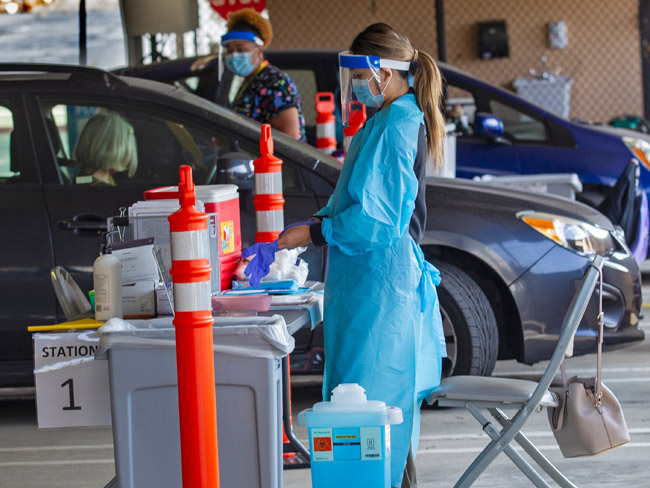 healthcare worker dressed in scrubs in front of cars lined up for drive-up COVID-19 testing