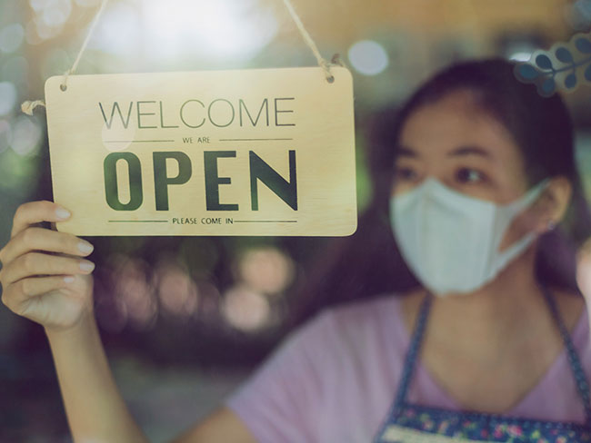 Asian woman with a mask on hold a business is open sign. 