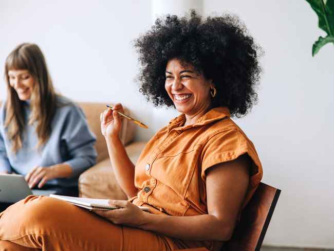 Black woman laughing while holding a pen and notebook