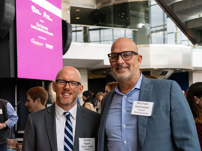 2 men standing together smiling at conference.