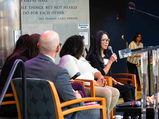 Speakers on stage with one holding the microphone talking.