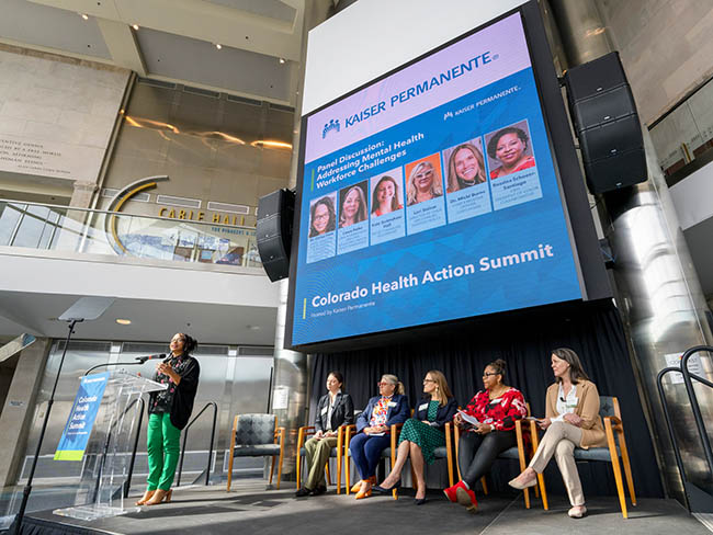 woman speaking to audience with a panelist behind her