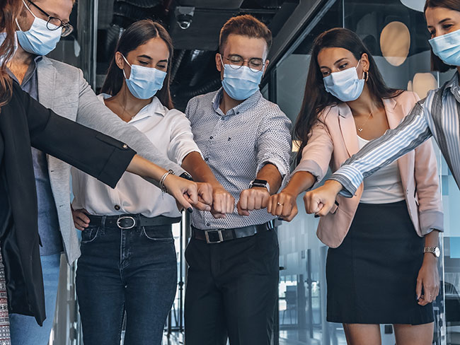 Group of colleagues wearing masks putting their fists all in