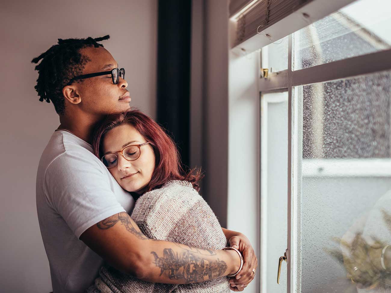 man hugging woman near a window where it's raining outside