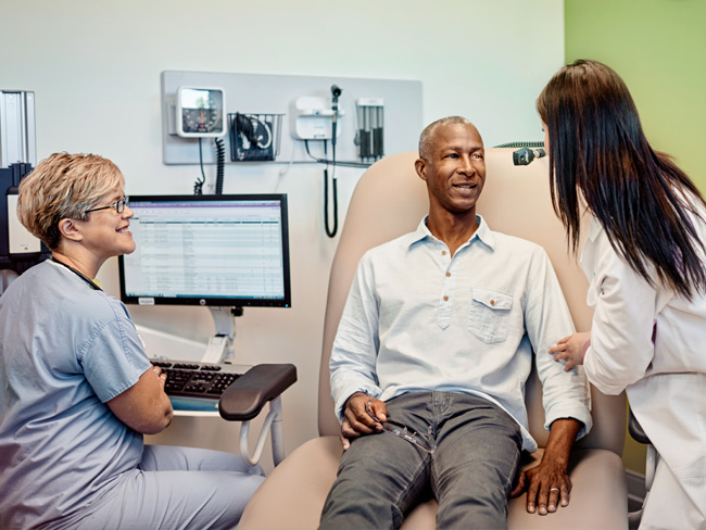 man sitting in exam room speaking with 2 medical professionals