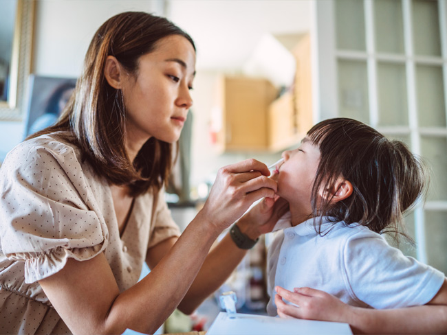 mother administering at-home covid-19 test to young girl