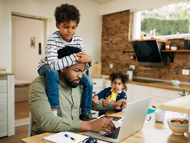 Busy dad working on a laptop while entertaining his kids