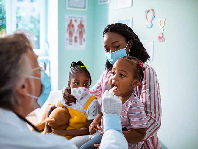 Mother and 2 daughters wearing face masks while one child is being examined by her physician