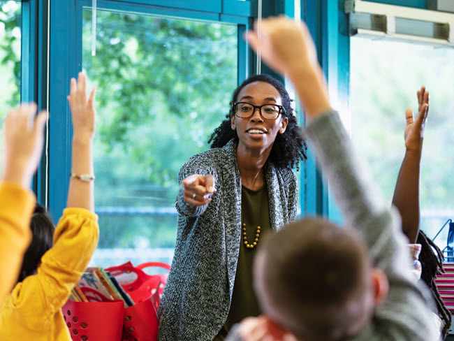 Teacher in classroom with students raising their hands.