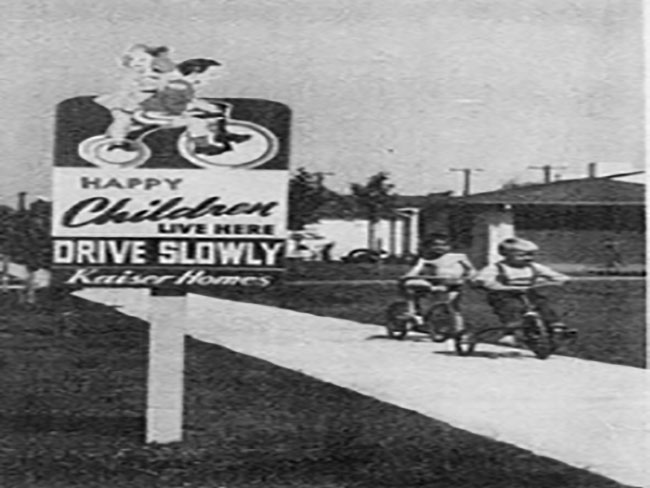 A Kaiser homes sign and 2 kids riding bikes