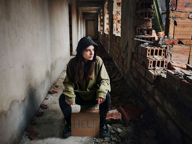 homeless teen sits in hallway with "HELP" sign