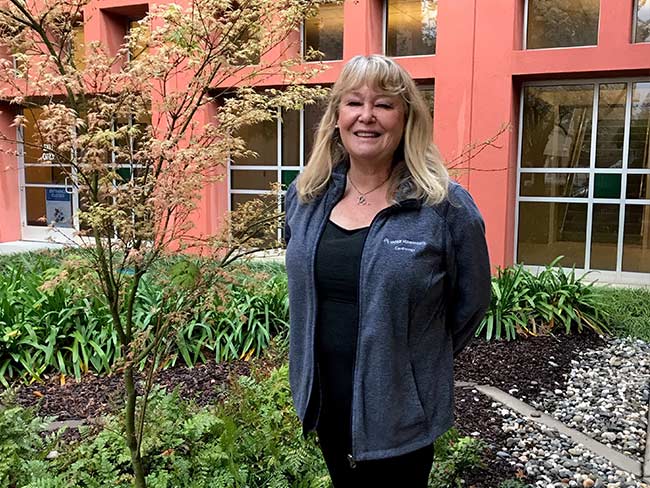 Woman stands in garden smiling. 