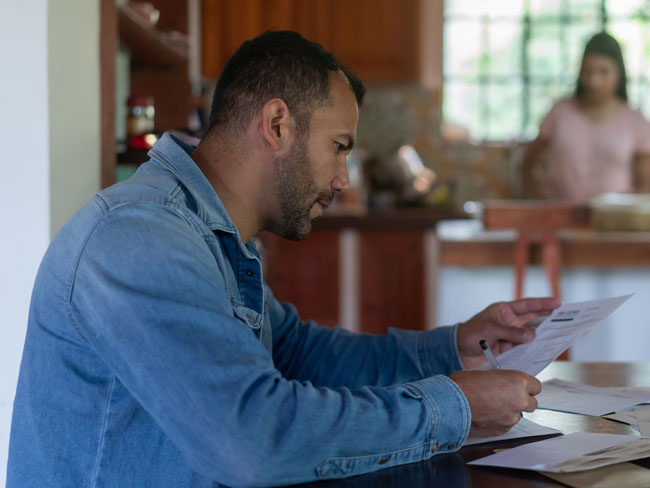 Man seated at a table looking concerned while looking through a stack of bills.