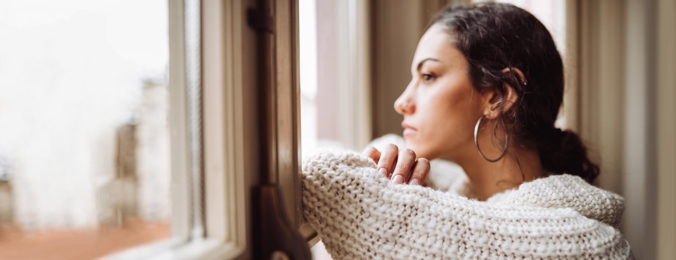 A young woman with arms folded, looking out a window.