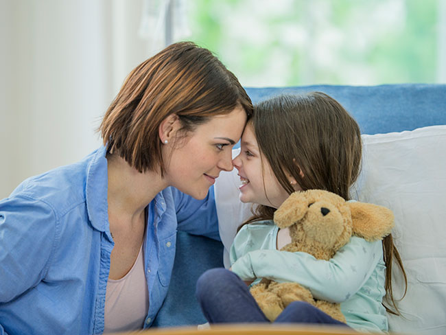 A woman and smiling child are rubbing their noses together 