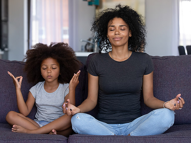 woman and young girl sitting on a sofa with their eyes closed meditating