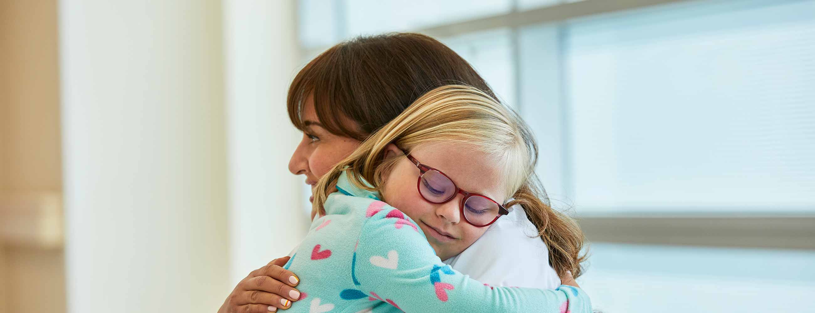 A female physician hugging a smiling pre-teen girl. 