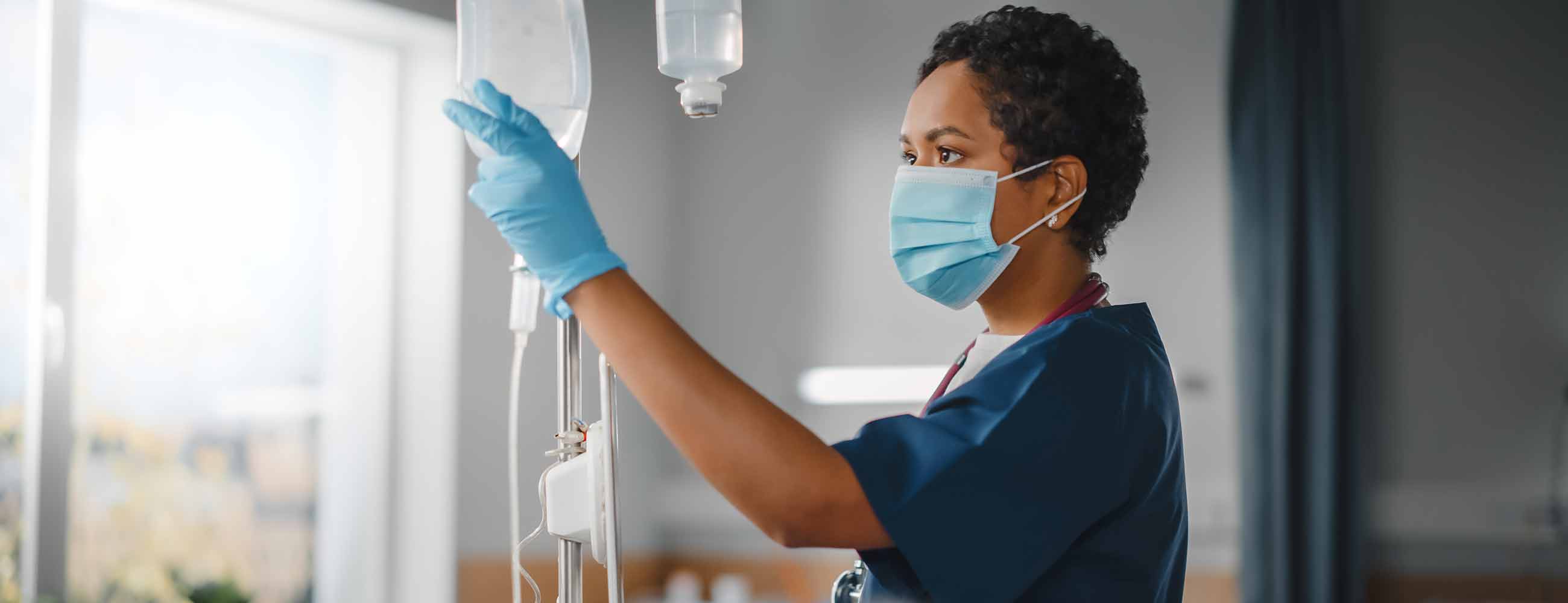 Black female nurse wearing face mask checking a patient's vitals