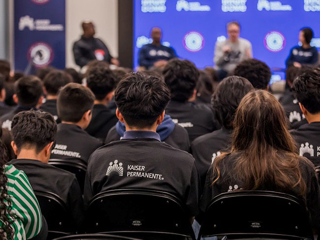 Back of heads facing blurred out panel of speakers