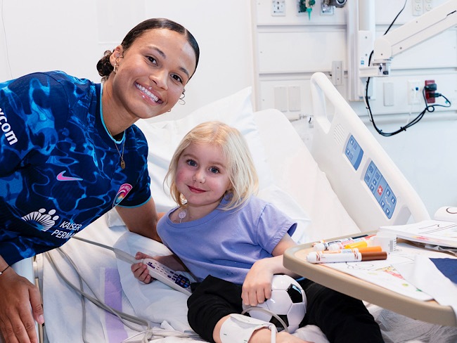 female soccer player with young girl smiling in a hospital room