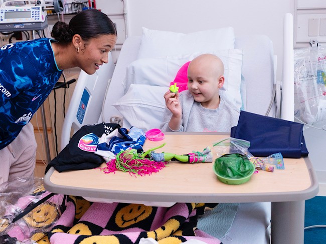female soccer player talking to girl in hospital bed with table full of toys
