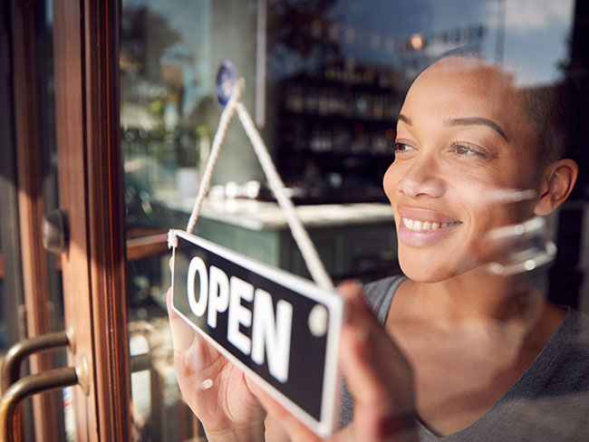 Female owner of a coffee shop turning around an open sign on the front door. 