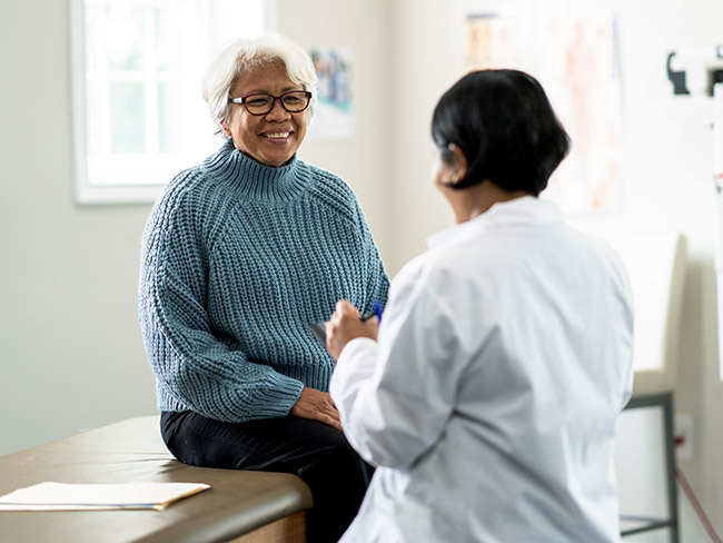 A senior woman sits up on the exam table at a doctors appointment.