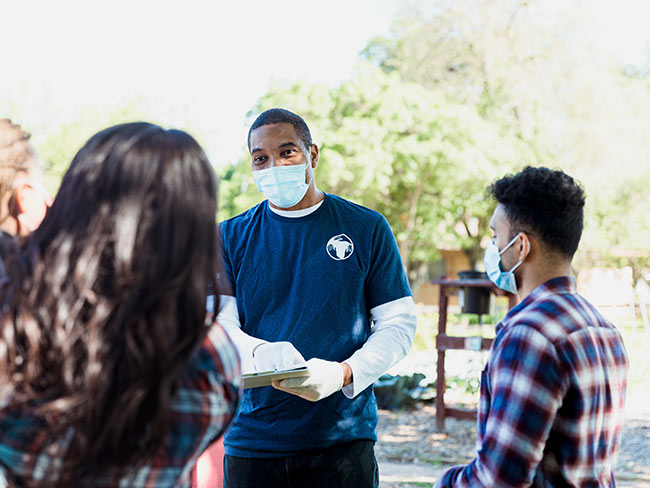 Man briefing a group of volunteers wearing face masks outdoors.