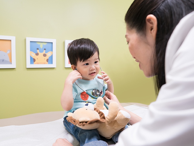 Child listens to stethoscope with doctor