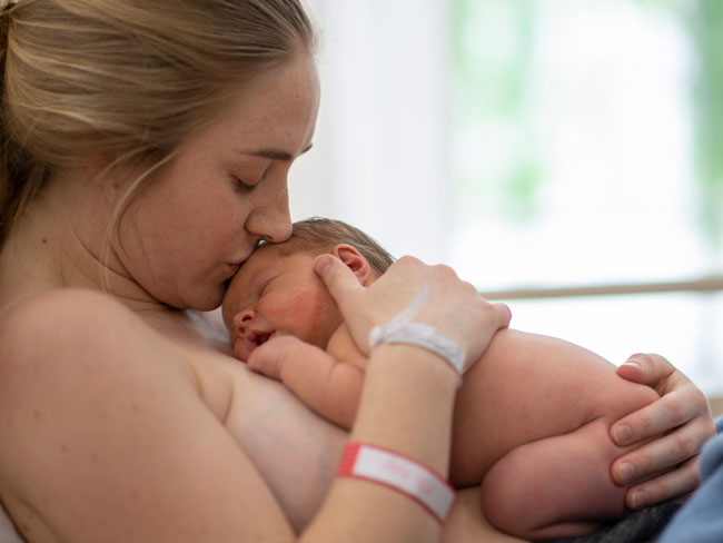 A new mother kisses newborn on forehead