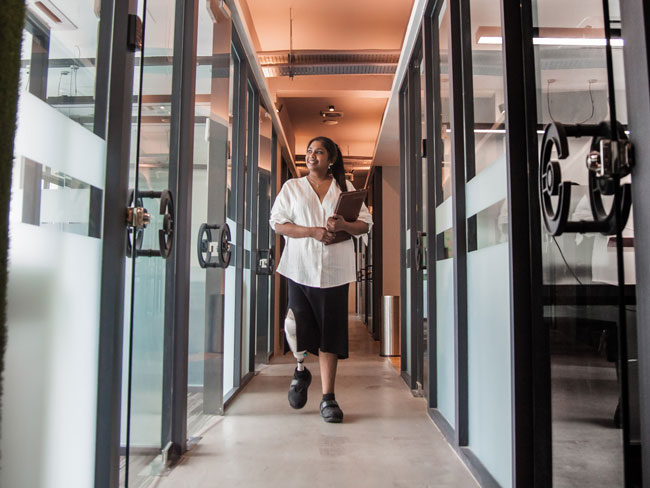 Asia Indian female handicapped businesswomen with prosthetic limb holding her digital tablet and walking at the office corridor