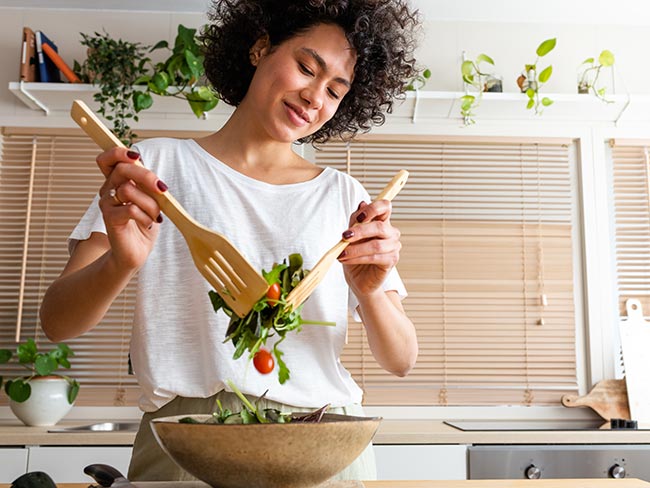 Woman tossing a salad in a brightly lit kitchen