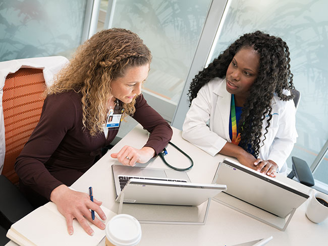 2 women are working with laptops at a table