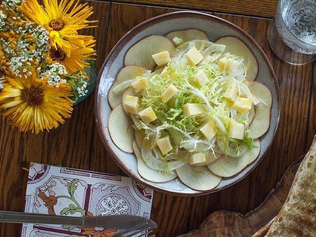 Shaved apple slices on plate, with fennel and Swiss cheese blocks on top