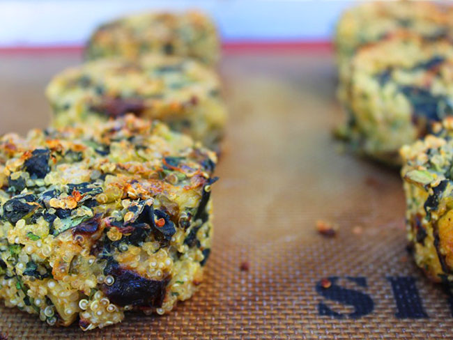 Quinoa cakes lined up on a silicone baking mat.