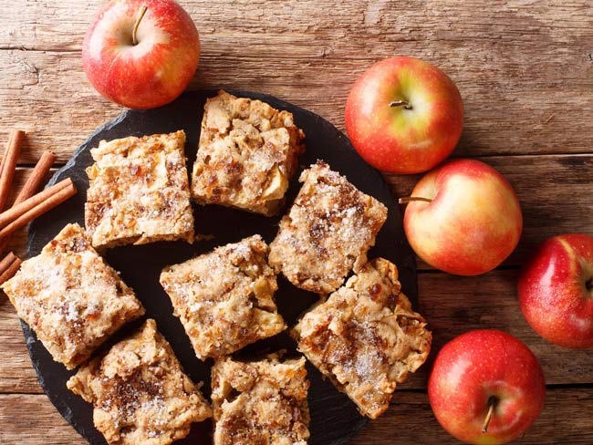 Overhead view showing square pieces of apple oatmeal pastry on plate, with apples place around plate.