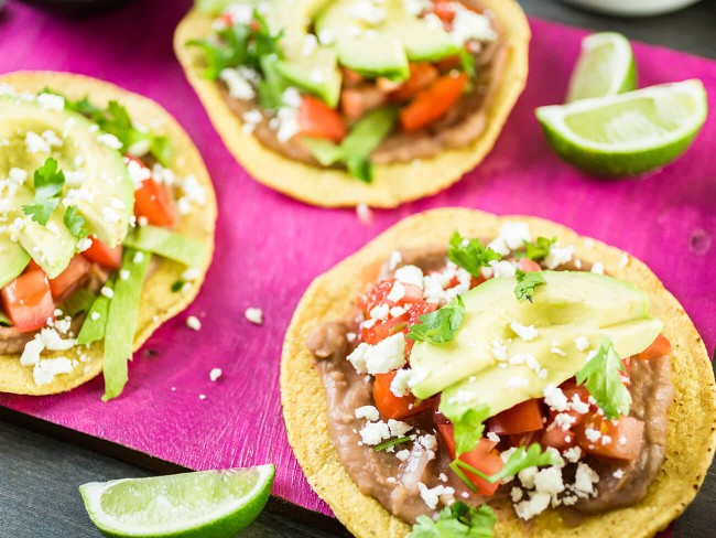 Black bean tostadas with salsa on a hot pink serving dish, surrounded by cut-up fresh limes.