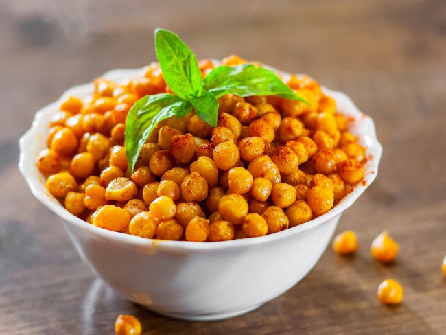 A big bowl of chickpea and peppadew salad with a sprig of oregano leaves on top. 