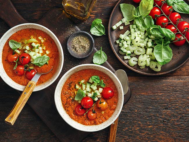 Bowl of chilled tomato soup with ingredients on a plate nearby