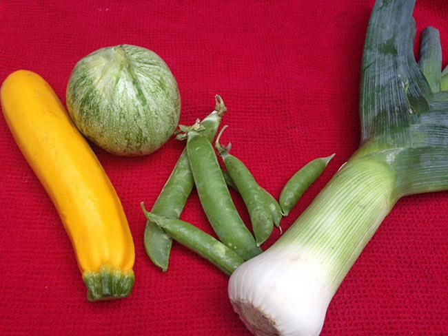 Leek zucchini and peas laid out on a red tablecloth 