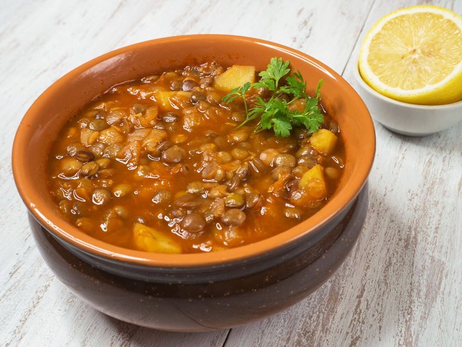 bowl of lentil soup with sweet potatoes and kale garnished with a sprig of parsley